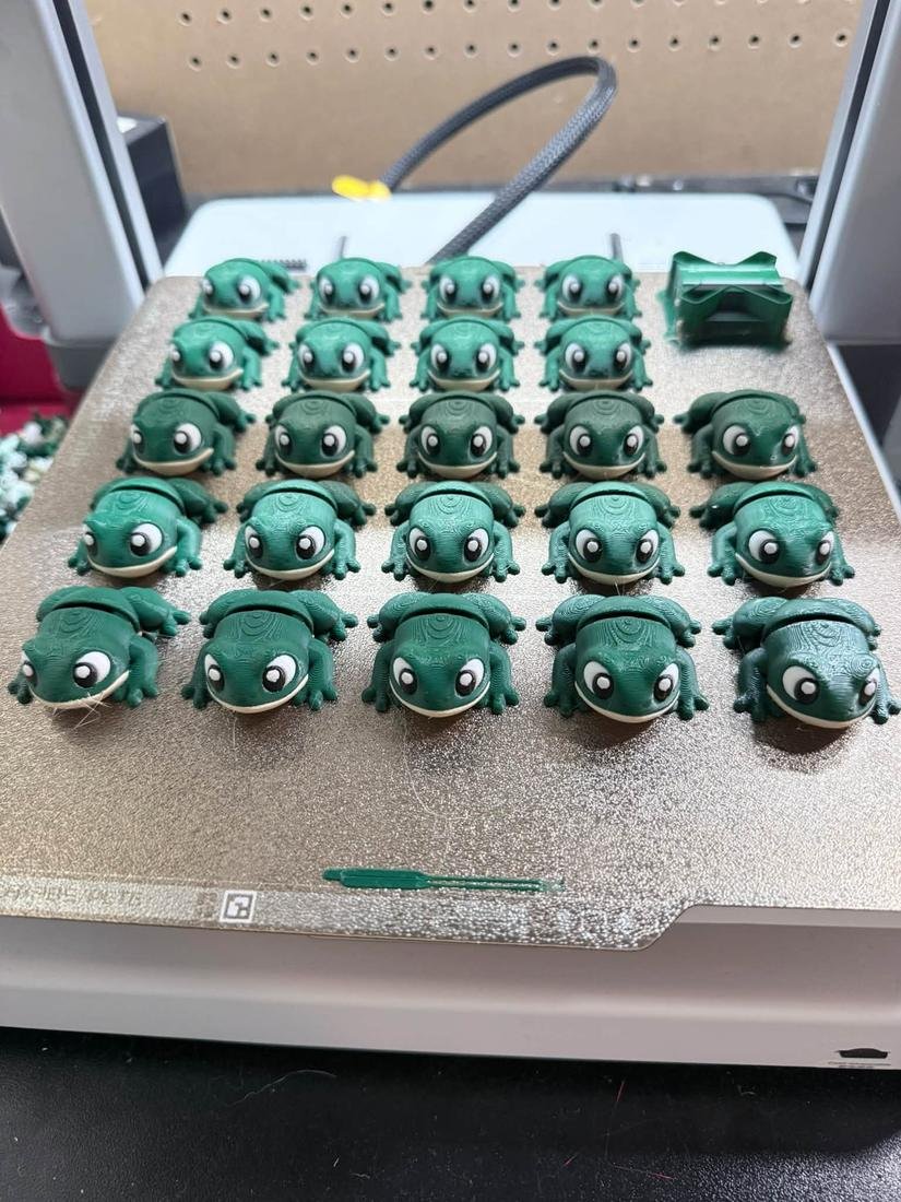 A print bed full of green 3D printed frogs